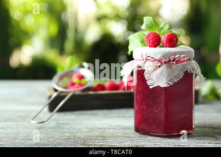 Glas Glas mit lecker Himbeermarmelade auf Tisch gegen Hintergrund verschwommen Stockfoto
