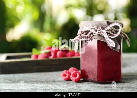 Glas Glas mit lecker Himbeermarmelade auf Tisch gegen Hintergrund verschwommen Stockfoto