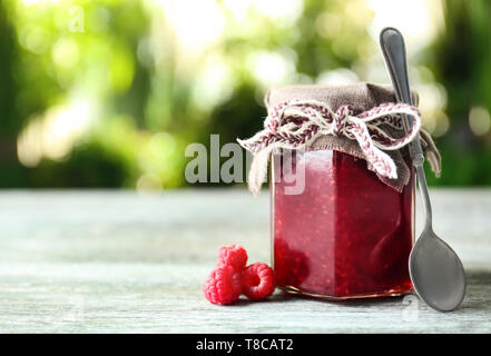Glas Glas mit lecker Himbeermarmelade auf Tisch gegen Hintergrund verschwommen Stockfoto