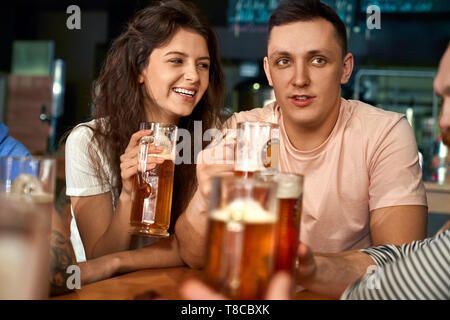 Vorderansicht des glücklichen Paar zusammen im Pub zu sitzen, Bier trinken und mit Freunden zu reden. Hübsche Frau und Mann Ruhe genießen, lachen und scherzen im Cafe. Konzept von Freizeit und Spaß. Stockfoto