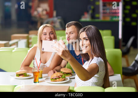 Attraktive junge Mädchen glücklich selfie zusammen mit Freunden im Cafe. Hübsche Mädchen und lustige junge Blick auf Kamera, lächeln und posieren während Rest. Konzept der Entspannung und Glück. Stockfoto