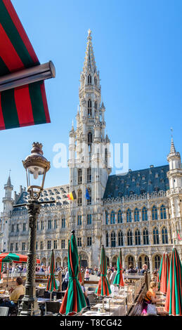 Touristen mit einem Drink auf der Terrasse eines Cafés auf dem Grand Place in Brüssel, Belgien, gegenüber dem Rathaus und der 96 Meter hohen Glockenturm. Stockfoto