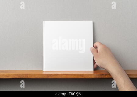 Konzept-man's Hand halten Quadratische weiße Notebook auf Regal und graue Wand für die Modellerstellung Stockfoto