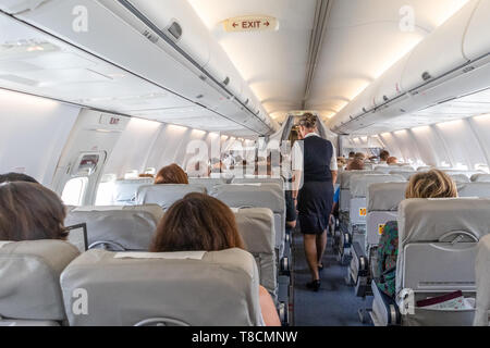 Innenraum der kommerziellen Flugzeugs mit einer Stewardess, die Passagiere auf den Sitzen während des Fluges. Stockfoto