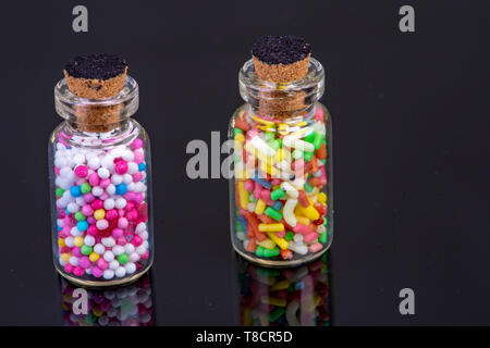 Glasflaschen mit buten Süßigkeiten gefüllt auf schwarzem Glas mit Spiegelung mit Korken Verschluss stehend Stockfoto