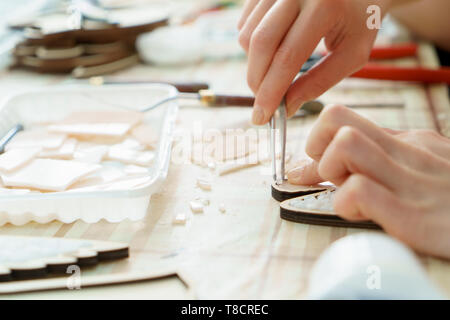 Der Künstler Teekocher Mosaik in einem hölzernen Ernte. Weibliche Hände closeup sammeln Mosaik aus bunten Steinen. Menschliche Aktivität am Arbeitsplatz Stockfoto