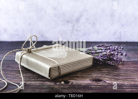 Handgefertigte Geschenk Konzept. Handwerk Papier recyceln Geschenkkarton mit Lavendel auf Holztisch. Im rustikalen Stil. Close-up. Stockfoto