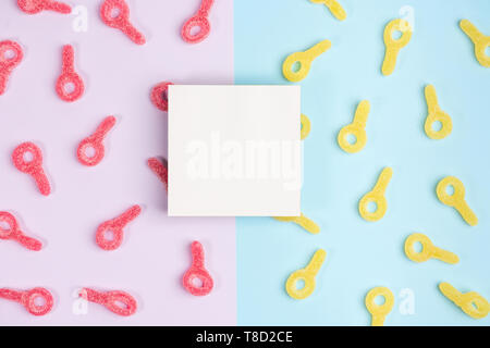 Leeres Blatt Papier auf dem Hintergrund der Gummibärchen Süßigkeiten. Bunte Bonbons auf Rosa und blauen Hintergrund. Ansicht von oben. Stockfoto