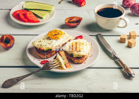 Sandwiches mit Gemüse und Spiegelei auf weissen Teller, Tasse Kaffee und einige Früchte über Holz- Hintergrund. Stockfoto