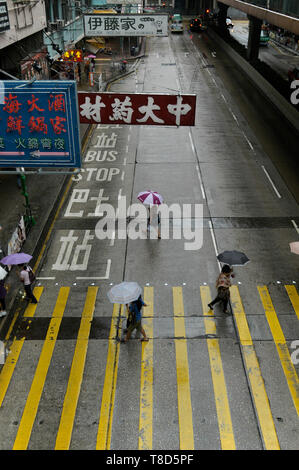 Menschen mit Schirmen das Überqueren einer Straße an einem regnerischen Tag in Hongkong, China Stockfoto