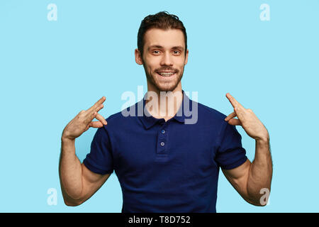 Mich an stilvollen jungen gutaussehenden Mann lächelt und zeigt auf seine blauen T-Shirt. Fashion Concept Stockfoto