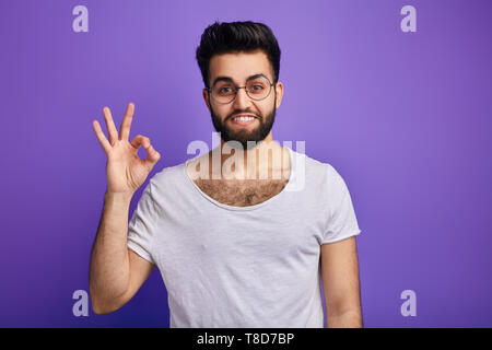 Wütend emotionaler Mensch zeigt Daumen hoch über blauen Hintergrund. bis Foto schliessen. Ja, ich habe es getan haben. Leistung. Kerl, der seine Ziele erreicht hat. Stockfoto