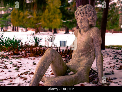 Eine steinerne Statue stellte vor einem gefrorenen Teich im Winter auf einem verschwommenen Hintergrund. Stockfoto