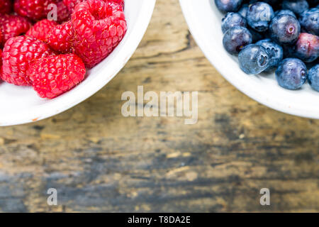 Horizontale Ansicht von frischem organischen Himbeeren und Blaubeeren in weißen Schalen auf einem braunen Holztisch Stockfoto