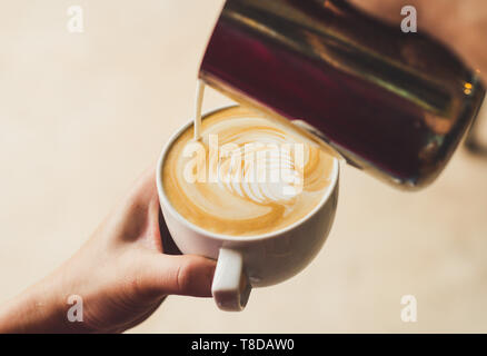 Closeup Bild der weiblichen barista Holding und Gießen Milch für bereiten Tasse Kaffee, latte Art, vintage Farbe Ton, Kaffee Zubereitung und Service conc Stockfoto