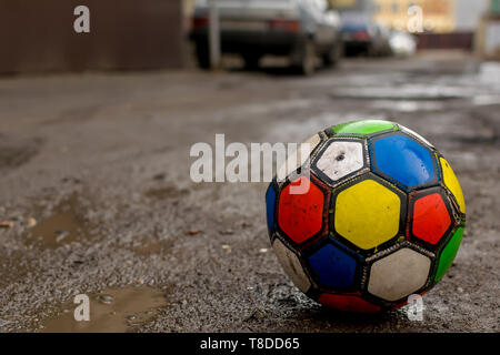 Fußball für Kinder ball spiel ist auf eine schmutzige kaputte Straße Straße unter Pfützen und wohnyards von Häusern, in der Nähe von geparkten Autos Stockfoto