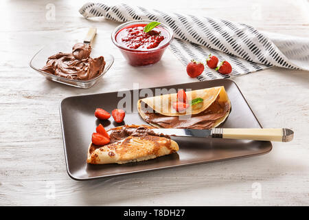 Leckere dünne Pfannkuchen mit Schokolade und Erdbeeren auf Platte Stockfoto