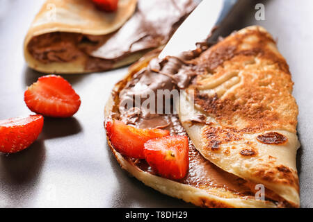 Leckere dünne Pfannkuchen mit Schokolade und Erdbeeren auf Platte, Nahaufnahme Stockfoto