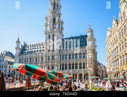 Touristen mit einem Drink auf der Terrasse eines Cafés auf dem Grand Place in Brüssel, Belgien, gegenüber dem Rathaus und der 96 Meter hohen Glockenturm. Stockfoto