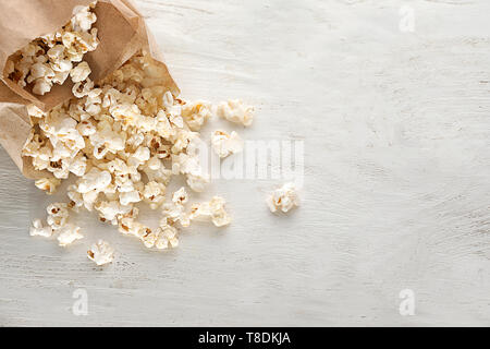 Papiertüten mit verstreuten leckeres Popcorn auf hölzernen Hintergrund Stockfoto