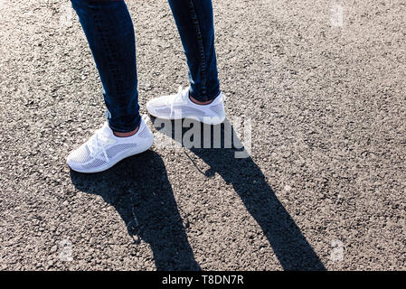 Frau in weißen Turnschuhen auf der Asphaltstraße in Richtung Sonne, aus der Nähe. Stockfoto