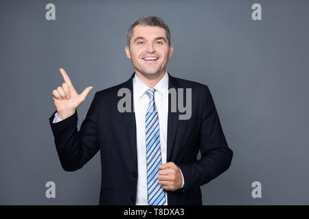 Gut aussehender Geschäftsmann mit erhobenem Zeigefinger auf grauem Hintergrund Stockfoto