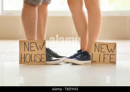 Die Beine des jungen Paares und Karton Blätter mit Text NEUES HAUS, NEUES LEBEN. Konzept der Umzug in neues Haus Stockfoto