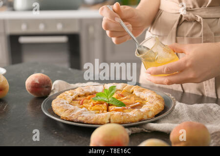 Frau gießen Honig auf köstlichen Pfirsich Galette am Tisch Stockfoto