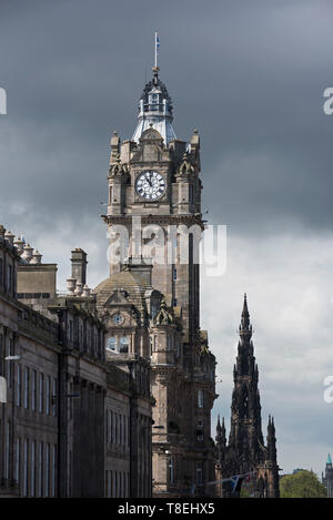 Der uhrturm der Balmoral Hotel an der Princes Street mit dem Scott Monument hinter einer bedrohlichen Himmel in der Ferne, Edinburgh, Schottland, Großbritannien und. Stockfoto