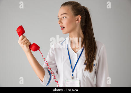 Foto von einer schönen jungen Frau cosmetologist Arzt über graue Wand Hintergrund sprechen per Telefon isoliert. Stockfoto