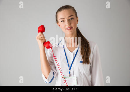 Foto von einer schönen jungen Frau cosmetologist Arzt über graue Wand Hintergrund sprechen per Telefon isoliert. Stockfoto