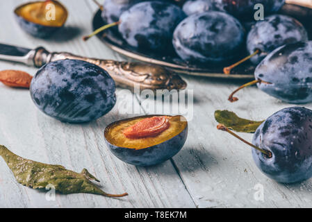 Reife Pflaumen mit in Scheiben geschnittenen Früchte, Blätter und vintage Messer über Licht Holz- Oberfläche Stockfoto