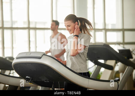 Athletische Frau im Fitnessstudio auf dem Laufband. Junge sportliche Frau mit Fitness tracker Armband beim aktiven Training im Fitnessraum. Genießen Sie die Trai Stockfoto