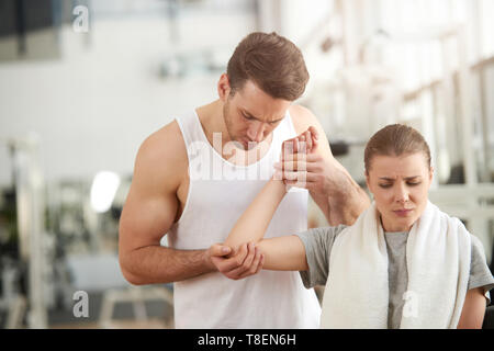 Man berühren weiblichen schmerzhafte Winkelstück am Gym. Junge hübsche Frau mit verletzte Hand erhalten erste Hilfe von Fitness Trainer in der Turnhalle. Sport Verletzungen der Ausübung Stockfoto