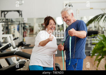 Ältere Frau, die ihre Ernährung Ziele zu feiern. Aufgeregt, ältere Frau, Maßband und zeigt mit dem Daumen nach oben. Sport und aktiv leben Konzept. Stockfoto