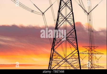 Hohe Spannung elektrische Pole und Übertragungsleitungen in den Abend. Strommasten bei Sonnenuntergang. Kraft und Energie. Energieeinsparung. Hohe Spannung gr Stockfoto