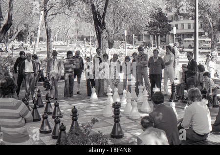 1977 Sydney Australien: Menschen, jung und alt, stand still und leise ein open air Schach Spiel mit Kniehohen Schachfiguren in Sydney's Hyde Park gespielt wird. Im Hintergrund eine Regierung Bus und anderen Verkehr bewegt sich Elizabeth Street. Das Schachbrett wurde Beton gemalt und die Stücke wurden von der Stadt zur Verfügung gestellt, Spiele wurden gemeinsame Wochentags mittags war und das ganze Wochenende. Stockfoto