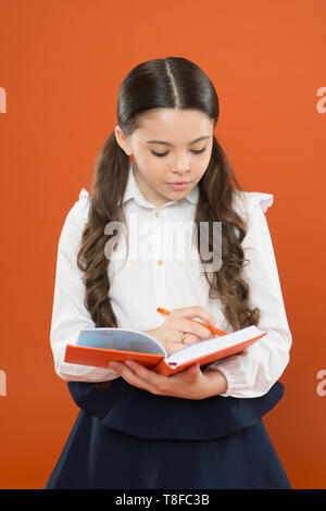 Schulmädchen Notizen auf orange Hintergrund. lesen Lektion. Angaben form Buch. zurück zu Schule. kleines Kind konzentrierte sich auf die Arbeit. kleine Mädchen in Schuluniform. Schreiben in der Arbeitsmappe. Stockfoto