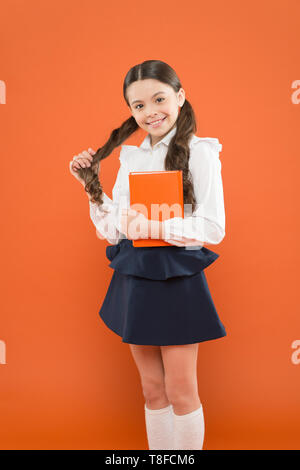 Lesen Lektion. Book Store Konzept. kleine Mädchen in Schuluniform. Angaben form Buch erhalten. Schulmädchen Notizen auf orange Hintergrund. zurück zu Schule. glückliches Kind. Zuversichtlich in ihr Wissen. Stockfoto