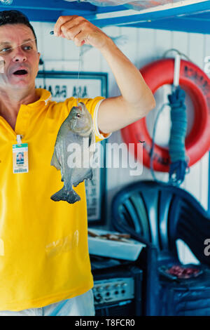 Santarem, Brasilien - Dezember 02, 2015: Aufgeregt Mann im gelben T-Shirt holding Fisch auf Linie. Die fischereitätigkeit Konzept. Aktiver Lebensstil und Hobby Stockfoto