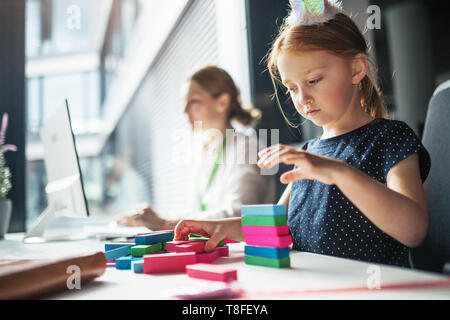 Eine Geschäftsfrau mit kleinen Tochter sitzt in einem Büro, arbeiten und spielen. Stockfoto