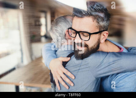 Ein erwachsener hipster Sohn und Vater in Innenräumen zu Hause, umarmen sich. Stockfoto