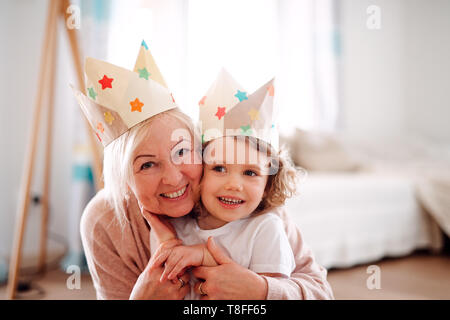 Ein Porträt von kleinen Mädchen mit Großmutter umarmt zu Hause. Stockfoto