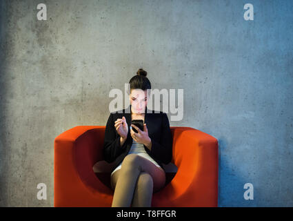 Eine junge geschäftsfrau mit Smartphone sitzen auf roten Sessel im Amt. Stockfoto
