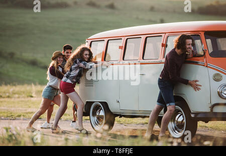 Eine Gruppe junger Freunde drücken ein kaputtes Auto auf einem Roadtrip durch die Landschaft. Stockfoto