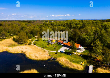 Kleines Dorf am Meer von oben an einem sonnigen Frühlingstag gesehen. Land, Straße, Wicklung zu den Häusern aus dem Wald. Meer mit Schilfrohr und Private Jet Stockfoto