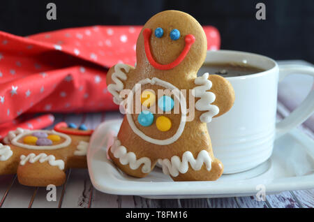 Weiße Tasse Tee mit einem Gingerbread Man cookie, ein weiteres Gingerbread Man mit schönen bunten Zucker in der Nähe, rot markierten Weihnachten Stoff Vereisung, wh Stockfoto