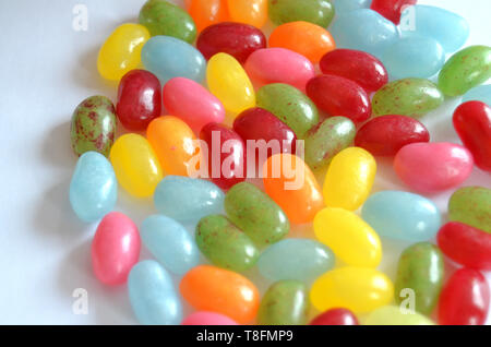 Verschiedene süße und saure Bunte Jelly Beans Bonbons mit verschiedenen Fruchtaromen, liegend auf einer weissen Fläche Stockfoto