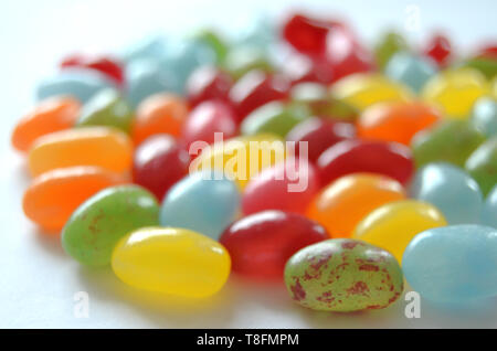 Verschiedene süße und saure Bunte Jelly Beans Bonbons mit verschiedenen Fruchtaromen, liegend auf einer weissen Fläche Stockfoto