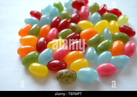 Verschiedene süße und saure Bunte Jelly Beans Bonbons mit verschiedenen Fruchtaromen, liegend auf einer weissen Fläche Stockfoto